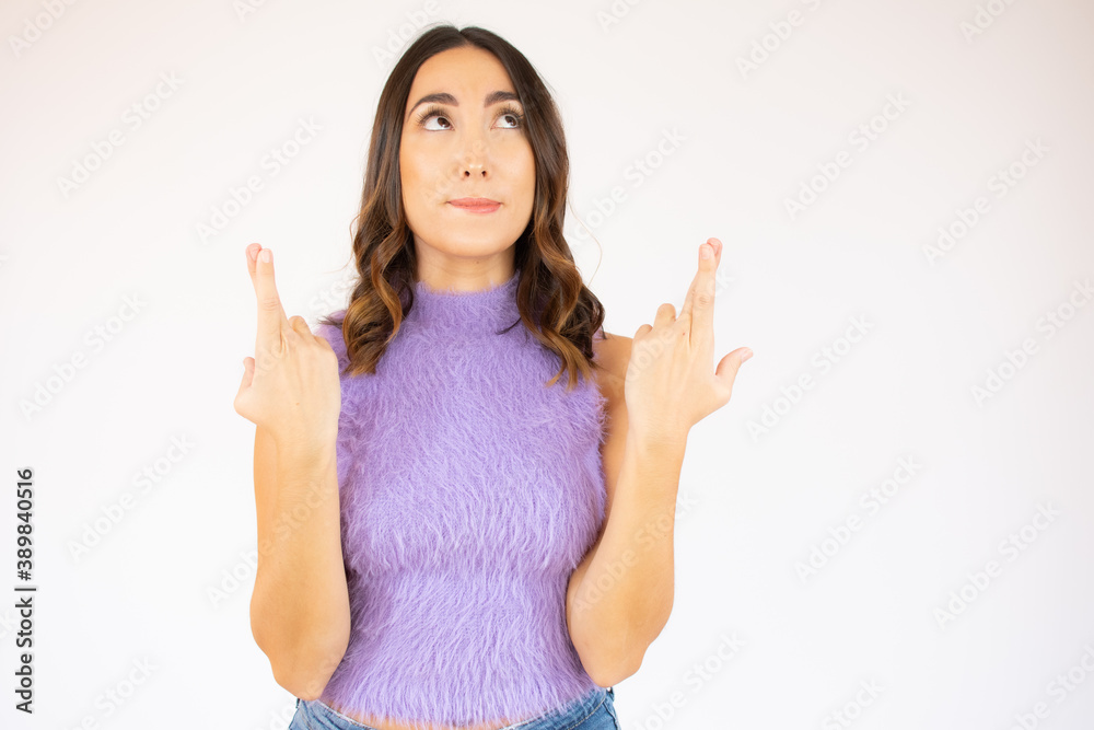 Portrait of a smiling young woman with brunette hair standing over white background, holding fingers crossed for good luck