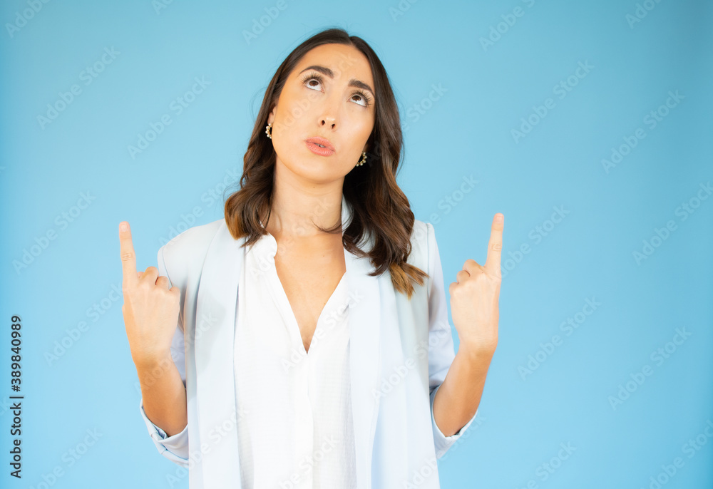Portrait of a happy young woman pointing fingers up at copy space isolated over blue background Portrait of a happy young woman pointing fingers up at copy space isolated over blue background