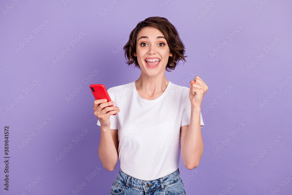 Photo portrait of cheerful happy girl with bob hair holding cellphone gesturing like winner isolated on vibrant purple color background Photo portrait of cheerful happy girl with bob hair holding cellphone gesturing like winner isolated on vibrant purple color background