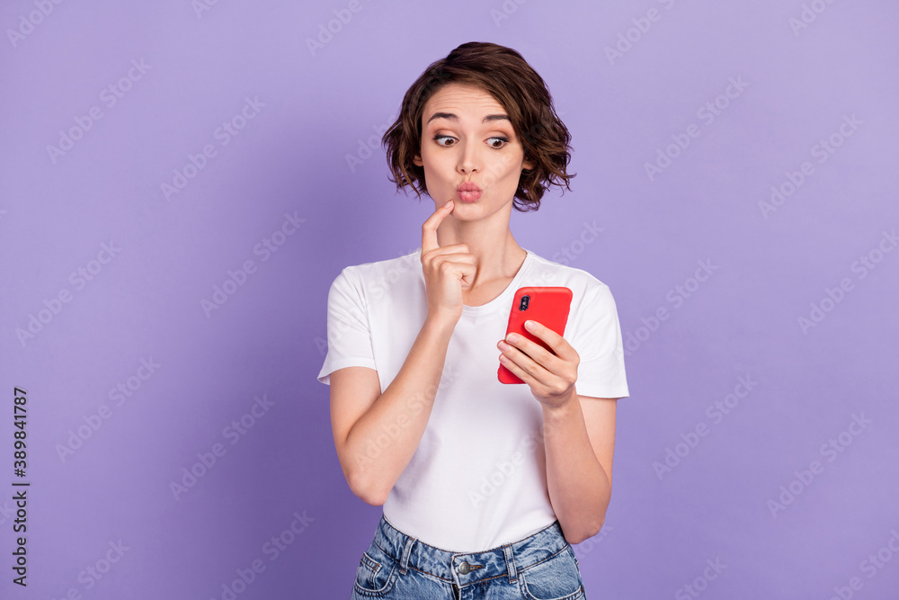 Photo portrait of interested girl with bob hair staring at cellphone touching chin pouted lips isolated on vibrant purple color background Photo portrait of interested girl with bob hair staring at cellphone touching chin pouted lips isolated on vibrant purple color background