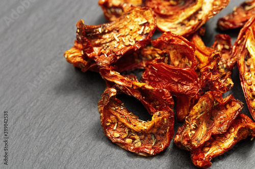 Sun dried tomatoes slices with Italian herbs and spices on dark background. Homemade dehydrated vegetable.
