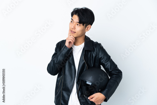 Chinese man with a motorcycle helmet isolated on white background thinking an idea while looking up