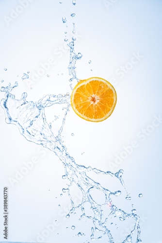 Half of orange fruit with water splash in midair, isolated on light blue background