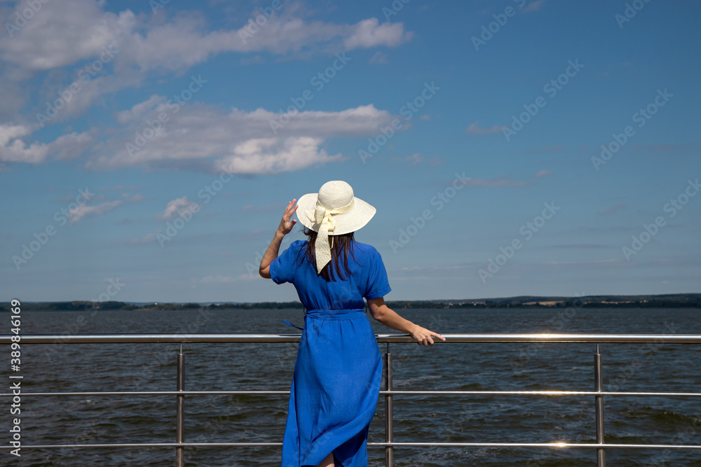 Young woman in hat stay back view on pier in stylish elegant dress poses enjoying amazing view.