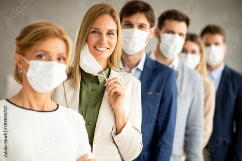 Business woman taking off her protective facial mask and looking at the camera with her team members standing in the line