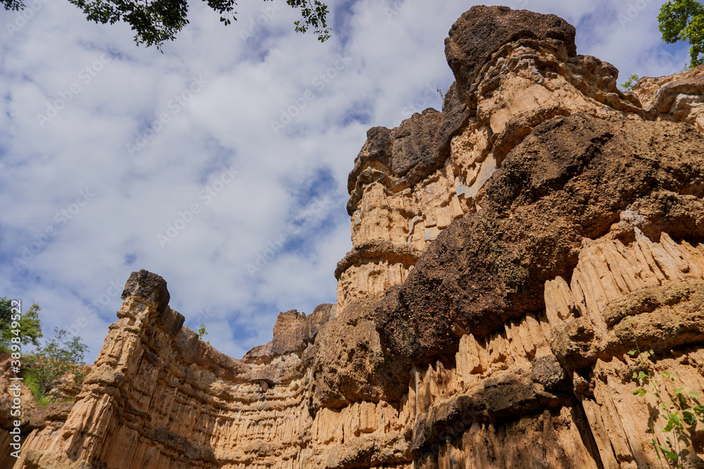 Fototapeta premium Look up shot Landscape corroded ancient natural curve cliff mountain from the rain up in the hill, with light brown colour and beautiful abstract pattern, blue clouds sky with leaves in the background