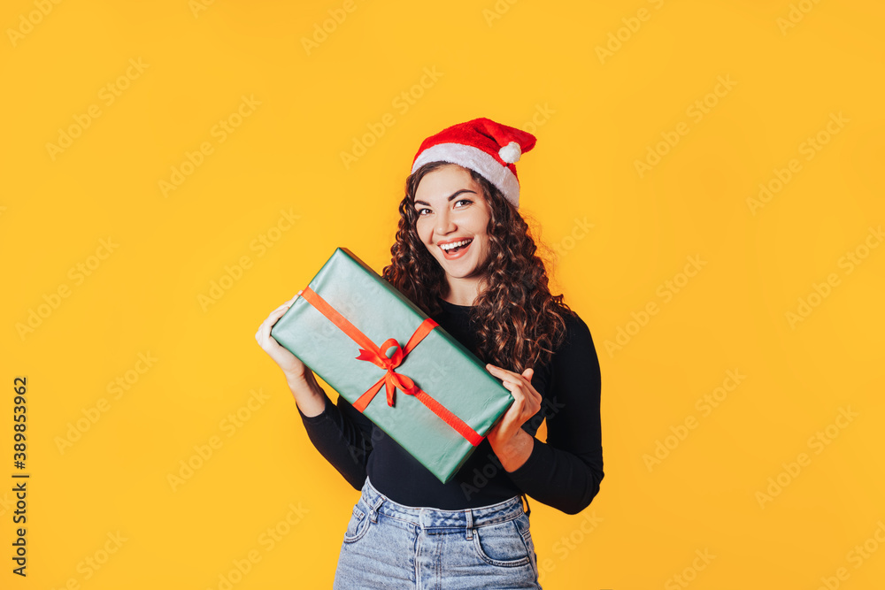 Woman holding box in green packaging with gift. Red santa hat is on his head. Expectation of presents for Christmas and new year. Place for your text Woman holding box in green packaging with gift. Red santa hat is on his head. Expectation of presents for Christmas and new year. Place for your text