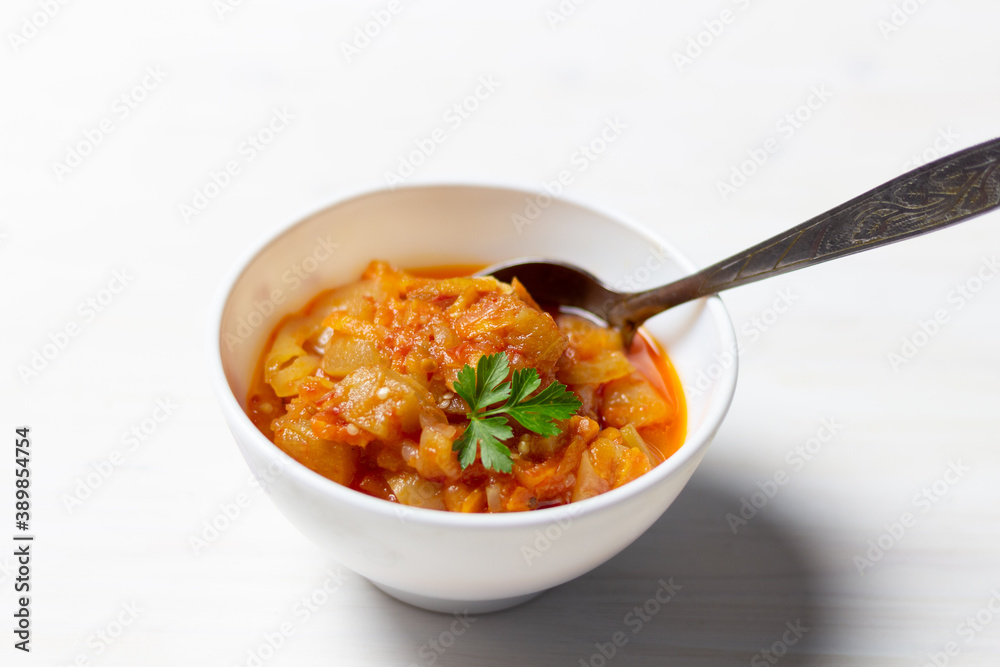 Eggplant appetizer with onion, oil, tomato, garnished with parsley in bowl with spoon on white background Eggplant appetizer with onion, oil, tomato, garnished with parsley in bowl with spoon on white background