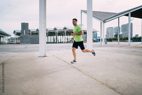 Determined man with smartphone and earphones jogging
