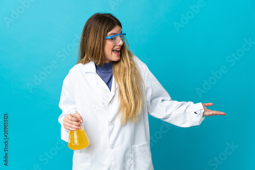 Young blonde scientific woman isolated on blue background with surprise expression while looking side