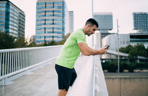 Serious ethnic sportsman using smartphone on bridge