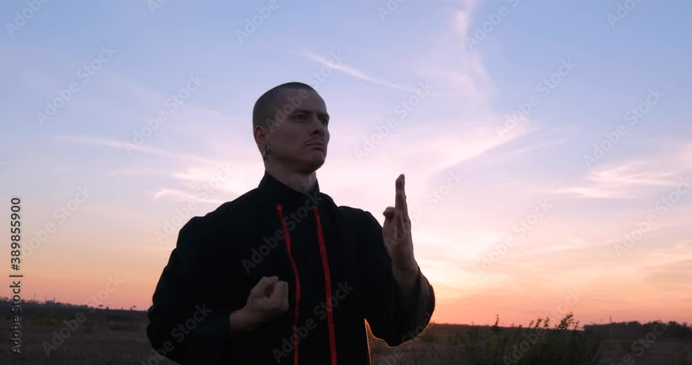 Silhouette of young male kung fu fighter practising alone in the fields during sunset 