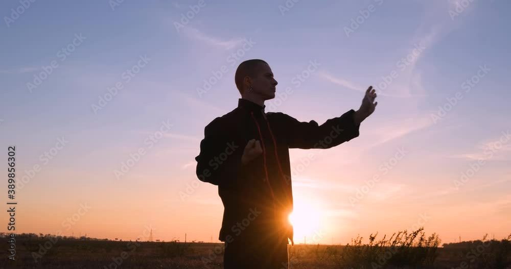 Silhouette of young male kung fu fighter practising alone in the fields during sunset 