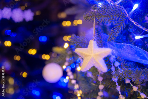 White star hanging on a Christmas tree, Christmas ornaments at night, white and gold holiday lights
