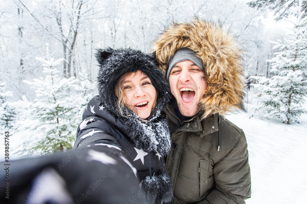Technologies and relationship concept - Happy smiling couple taking a selfie in a winter forest outside