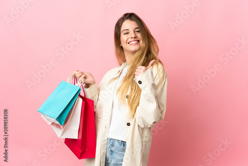 Young woman with shopping bag isolated on pink background holding shopping bags and with thumb up
