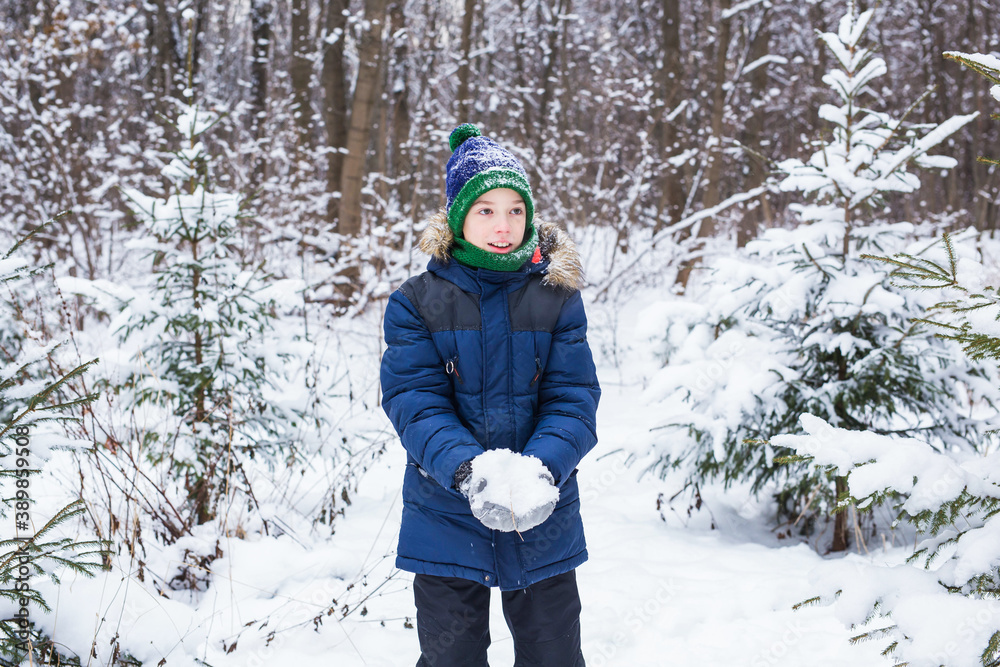 Cute young boy plays with snow, have fun, smiles. Teenager in winter park. Active lifestyle, winter activity, outdoor winter games, snowballs.