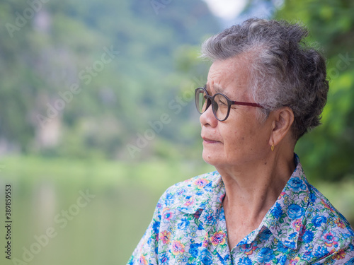 Side view of an elderly Asian woman smiling and looking away while standing in the park. Concept of aged people and healthcare