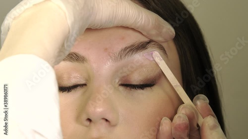 Correction of a shape of eyebrows with hot wax close up. Brow master applying wax on the eyebrow of female face of a brunette woman. Wax correction of the shape of the eyebrows with spatula. Beauty in