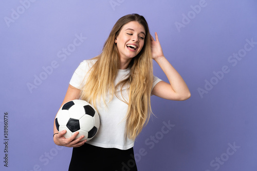 Young blonde football player woman isolated on purple background listening to something by putting hand on the ear © luismolinero