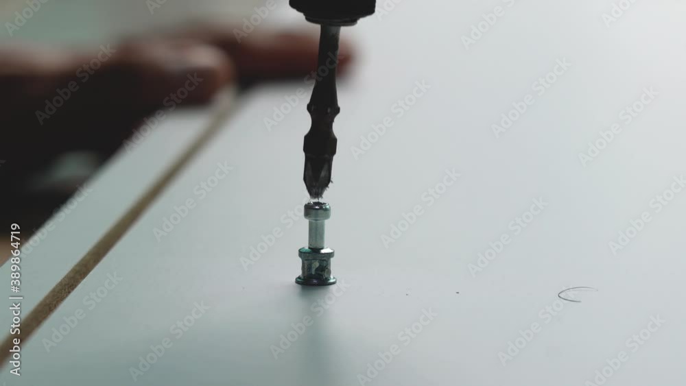 Power screwdriver is screw-in a iron bolt into wooden plank board during furniture assembly action. Close-up and selective focus, working 4K footage. Power screwdriver is screw-in a iron bolt into wooden plank board during furniture assembly action. Close-up and selective focus, working 4K footage.
