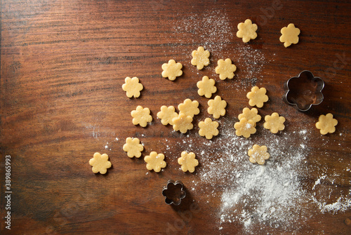 Small flower shape cookies, cookie-cutter and sprinkled floor scattered on the wooden background. Cookies are ready to be fried. photo
