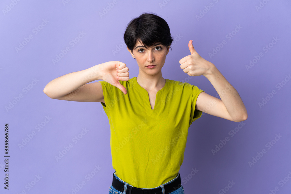 Woman with short hair isolated on purple background making good-bad sign. Undecided between yes or not Woman with short hair isolated on purple background making good-bad sign. Undecided between yes or not