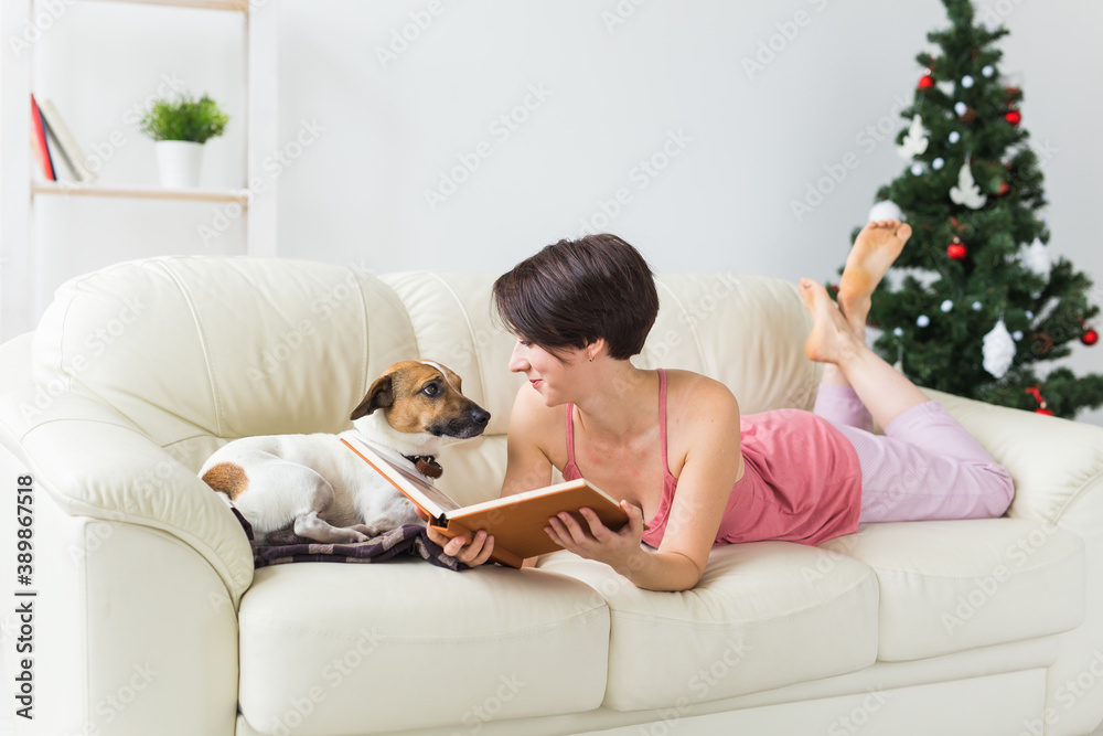 Woman reads book in front of Christmas tree with dog jack russell terrier. Christmas, holidays and pet. Woman reads book in front of Christmas tree with dog jack russell terrier. Christmas, holidays and pet.