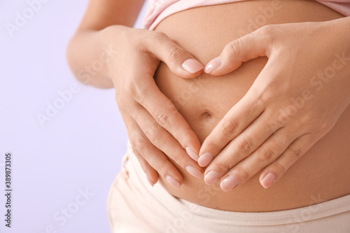 Beautiful pregnant woman making heart with her hands on color background, closeup
