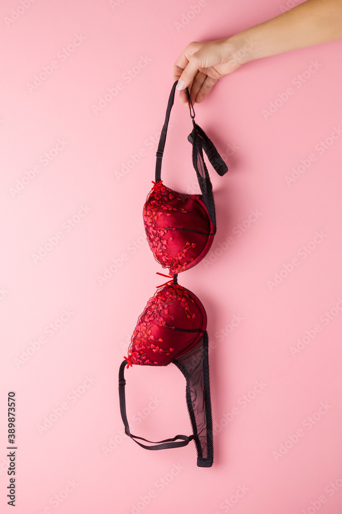 Foto de Young adult woman hand holding black red bra on light pink