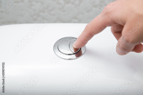 Young woman hand finger pushing button in toilet. Closeup. photo
