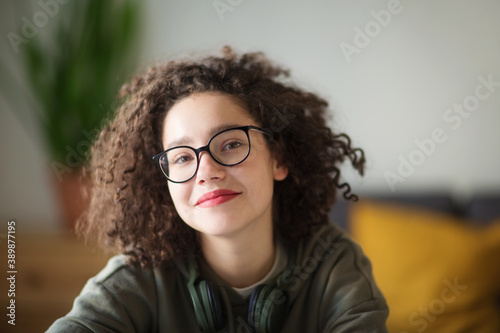 girl in glasses looks at camera and smiles. student talks over Internet. Video Conference or e-learning at home. portrait of person at wide angle.
