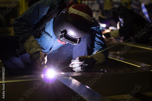 Welder is welding the steel in the factory. Weld the steel in dark. Workers wearing industrial uniforms and welding masks at a welding factory protect from welding sparks. Occupational safety concept