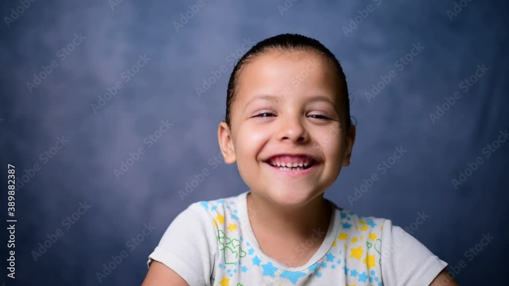 Confident smiling Brazilian girl looking at the camera while standing. Happy laughing. Child with white teeth cute face posing for close up portrait, blue background. Confident smiling Brazilian girl looking at the camera while standing. Happy laughing. Child with white teeth cute face posing for close up portrait, blue background.