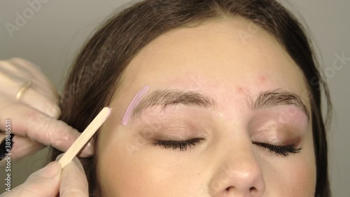 Correction of a shape of eyebrows with hot wax close up. Brow master applying wax on the eyebrow of female face of a brunette woman. Wax correction of the shape of the eyebrows.