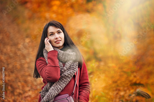 Attractive brunette woman talking on phone while walking in autumn park, walks against loneliness