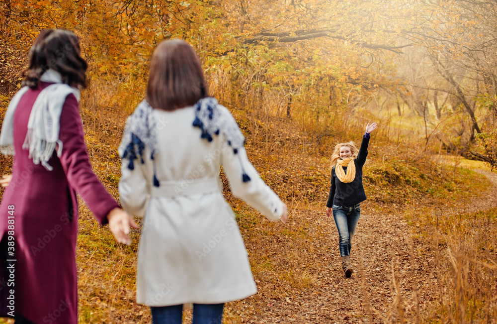 Two young women in autumn park greeting their girlfriend and keeping distance, getting rid of the autumn desires