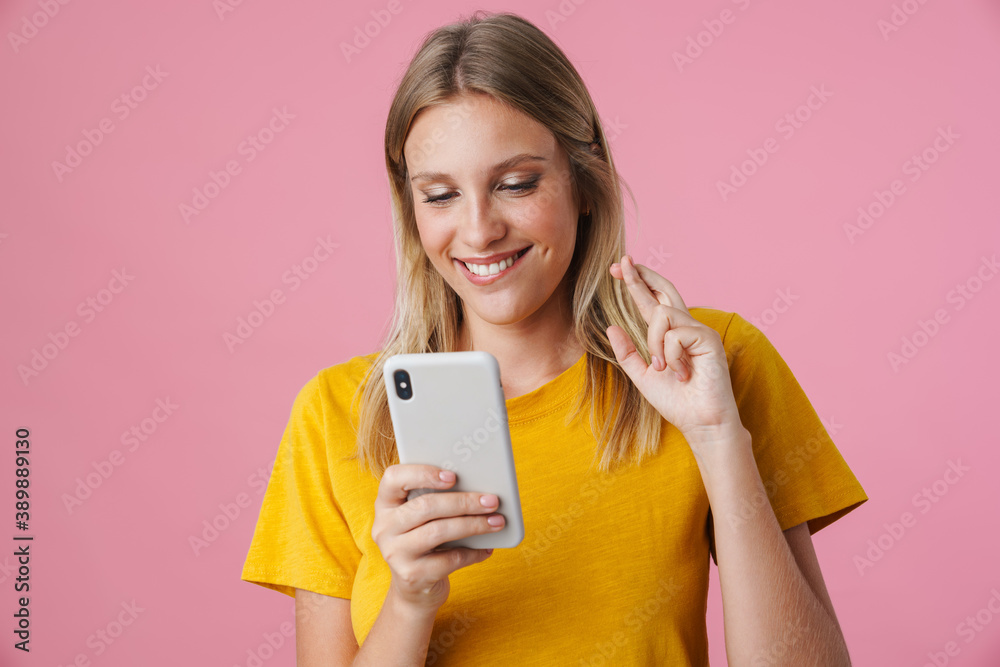 Cheerful blonde girl holding fingers crossed and using mobile phone Cheerful blonde girl holding fingers crossed and using mobile phone