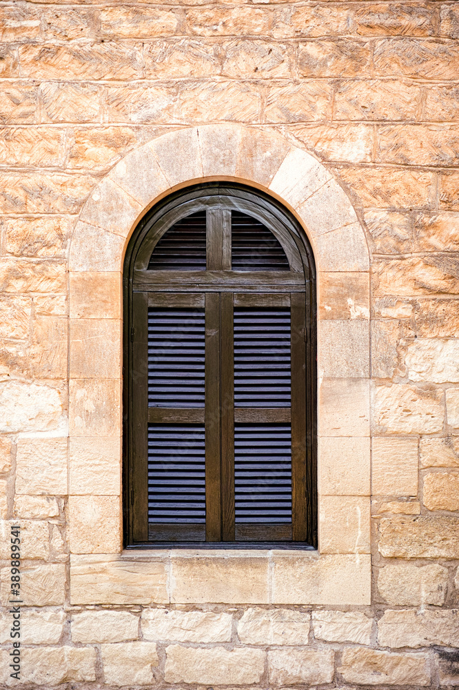 Arched window with closed shutters on stone wall