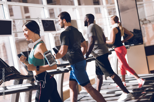 People walk on treadmill together in sports hall.