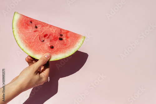 Feminine hand holding slice of ripe watermelon over pink backgroun