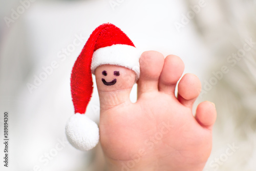 Child big toe with santa hat and smiling face.  Closeup photo of caucasian foot. Christmas and barefoot concept with copy space. © Michaela