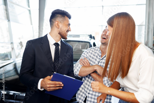 Man car salesman telling about the features of the new car to the couple