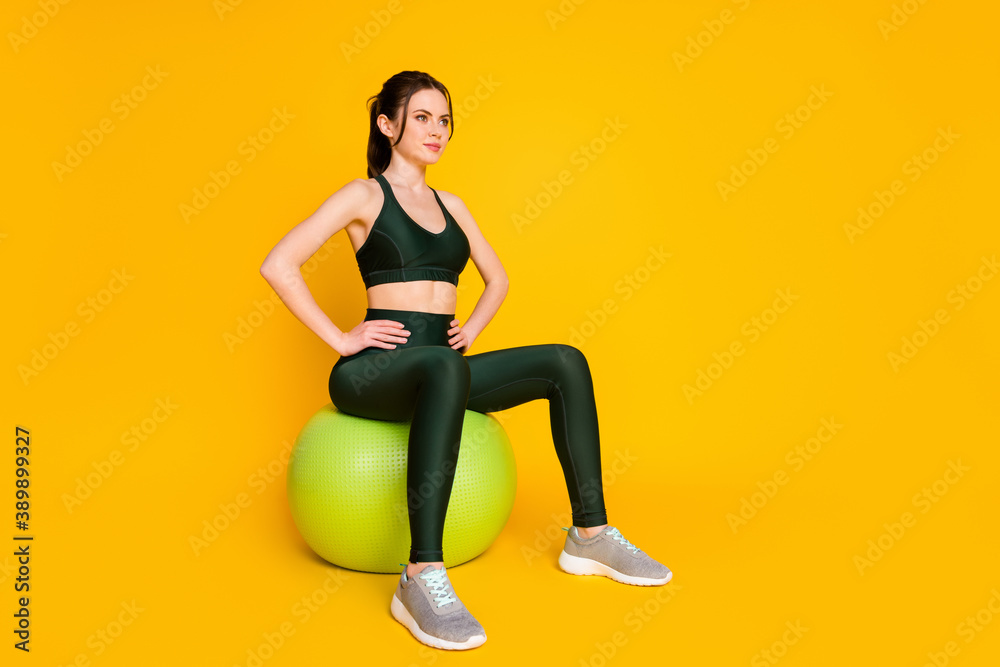 Fototapeta premium Full length photo of sportive lady sit big green fit ball focused wear suit top pants sneakers isolated yellow color background
