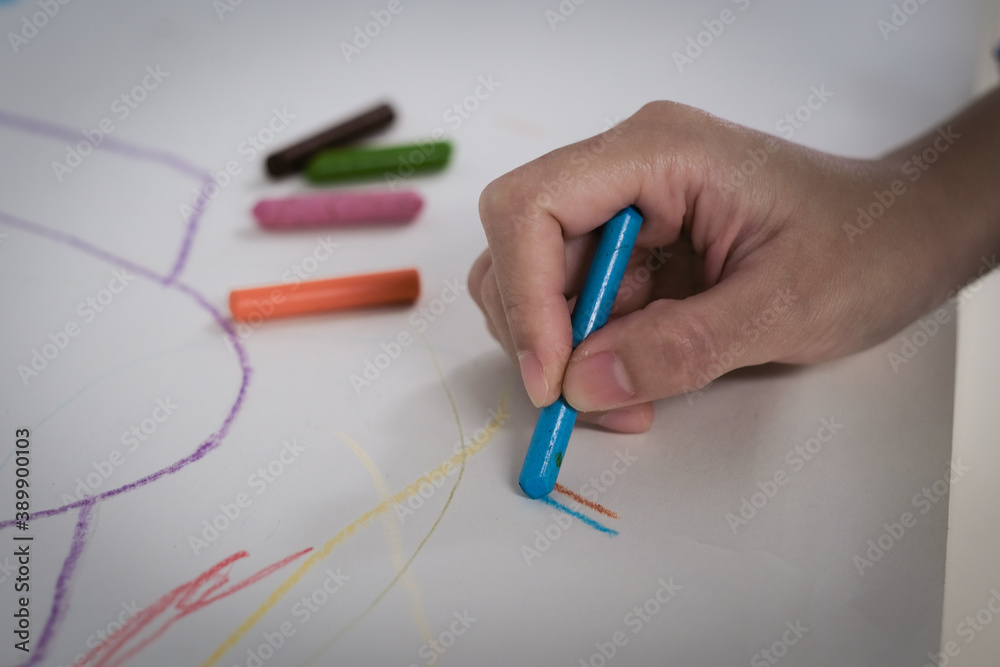 The child is painting with crayons on white paper.