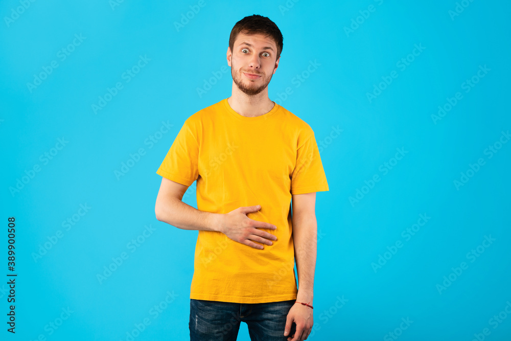 Young satisfied man touching his stomach at studio Young satisfied man touching his stomach at studio
