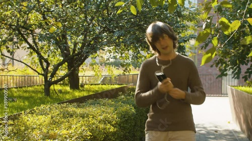 Funny hipster dancing in a park, holding smartphone in hands and listening to music through headphones. Autumn sunny day. Steadicam shot