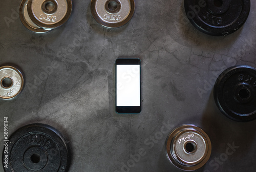 Mobile phone on a concrete surface with weight plates of different weights, sizes and colors with empty space
