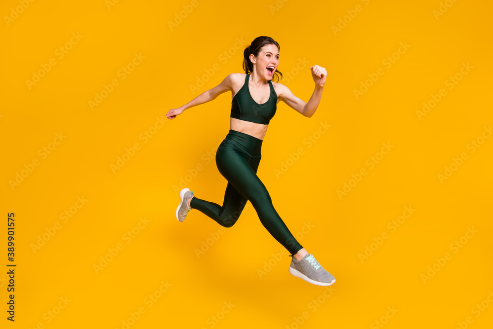 Cheerful lady jump high jogging marathon speed race competitive person wear sports suit shoes isolated yellow color background
