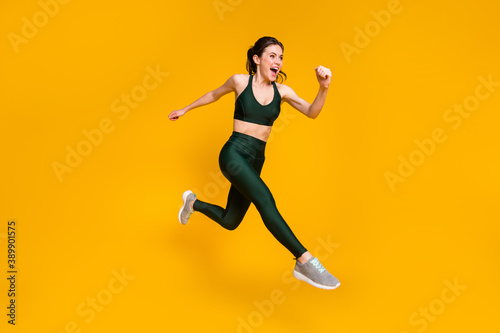 Cheerful lady jump high jogging marathon speed race competitive person wear sports suit shoes isolated yellow color background